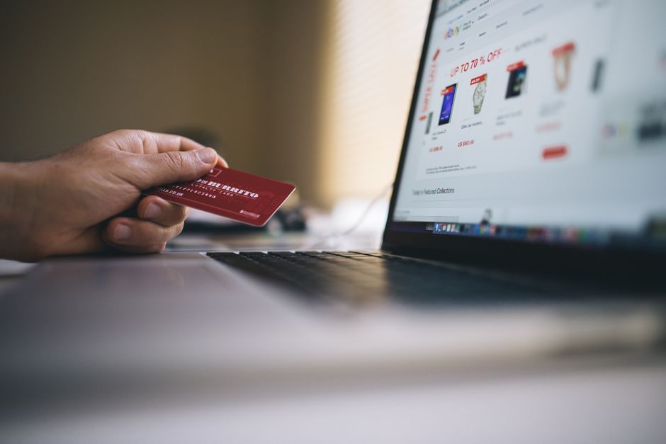 ノートパソコンで買い物をしながらクレジットカードを手にしている人