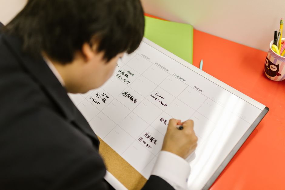 机の上でプランナーに書き込みながら、1週間の投稿予定を並べて整理している様子のイメージ画像